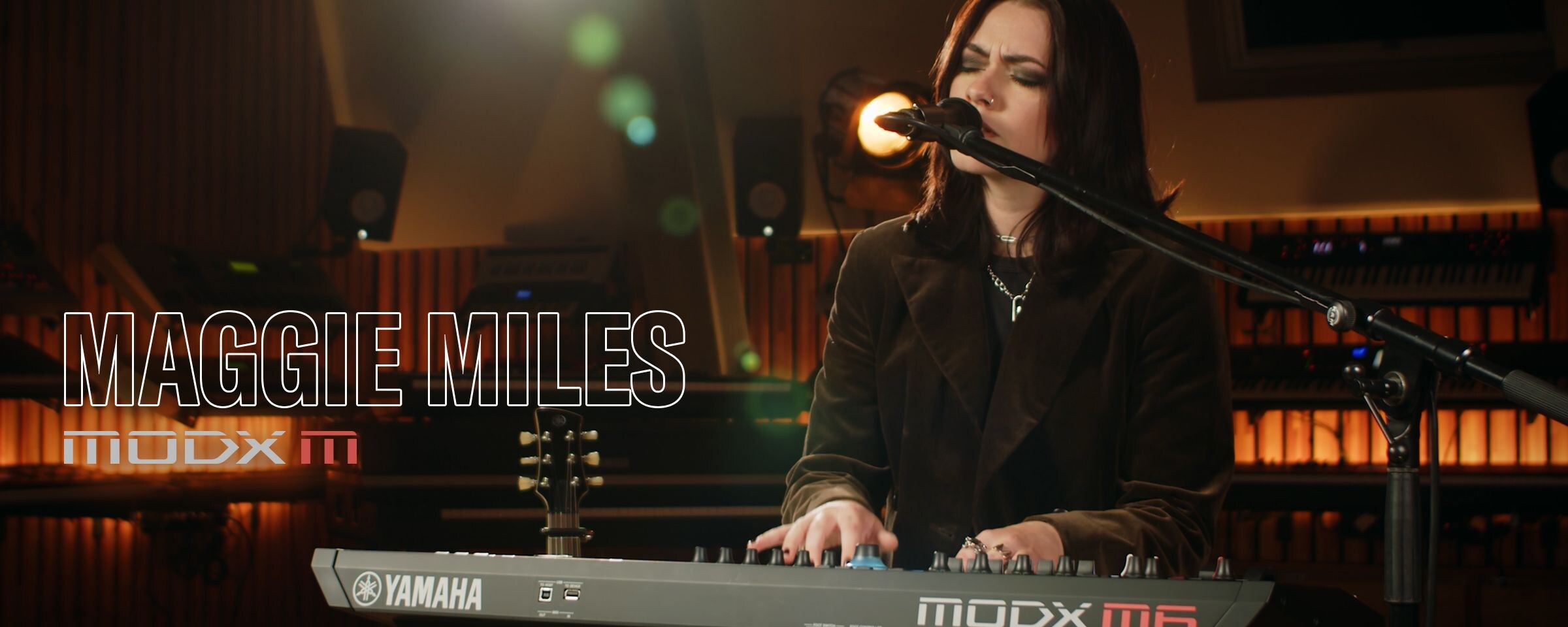 Visual of Maggie Miles singing while playing a synthesizer in a performance scene